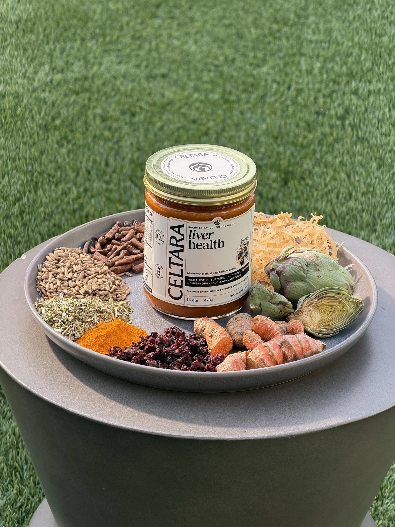 Jar of Celtara liver health supplement on a plate with herbs and vegetables outdoors.
