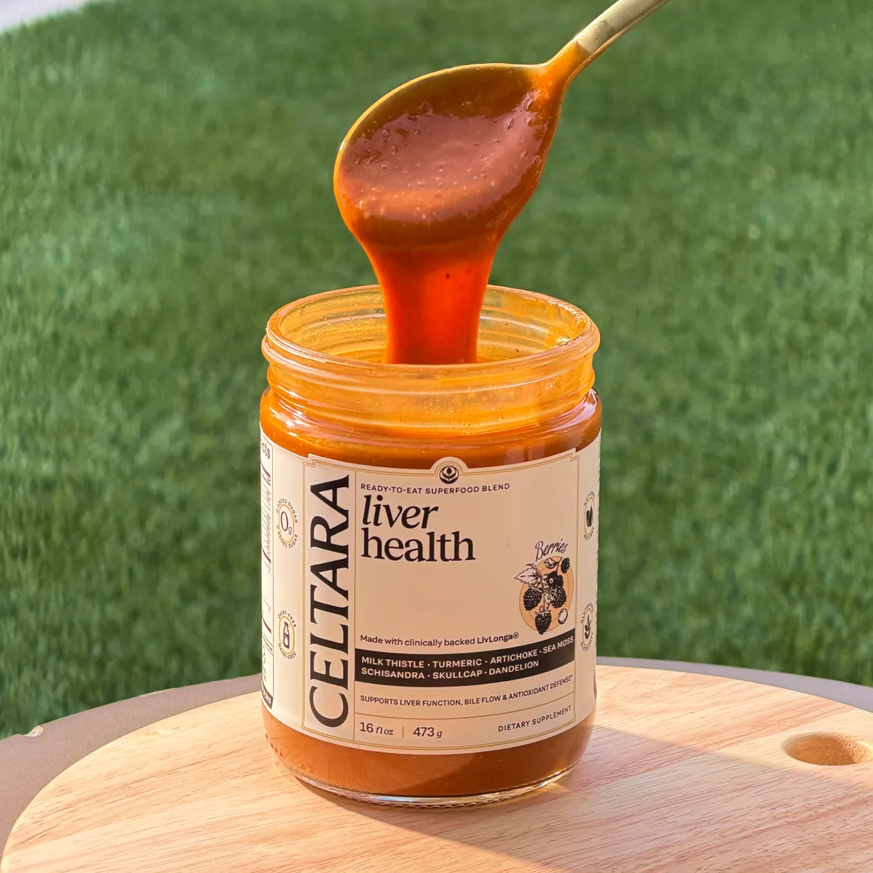 Jar of Celtara liver health supplement with a spoonful being lifted against a green grass background.