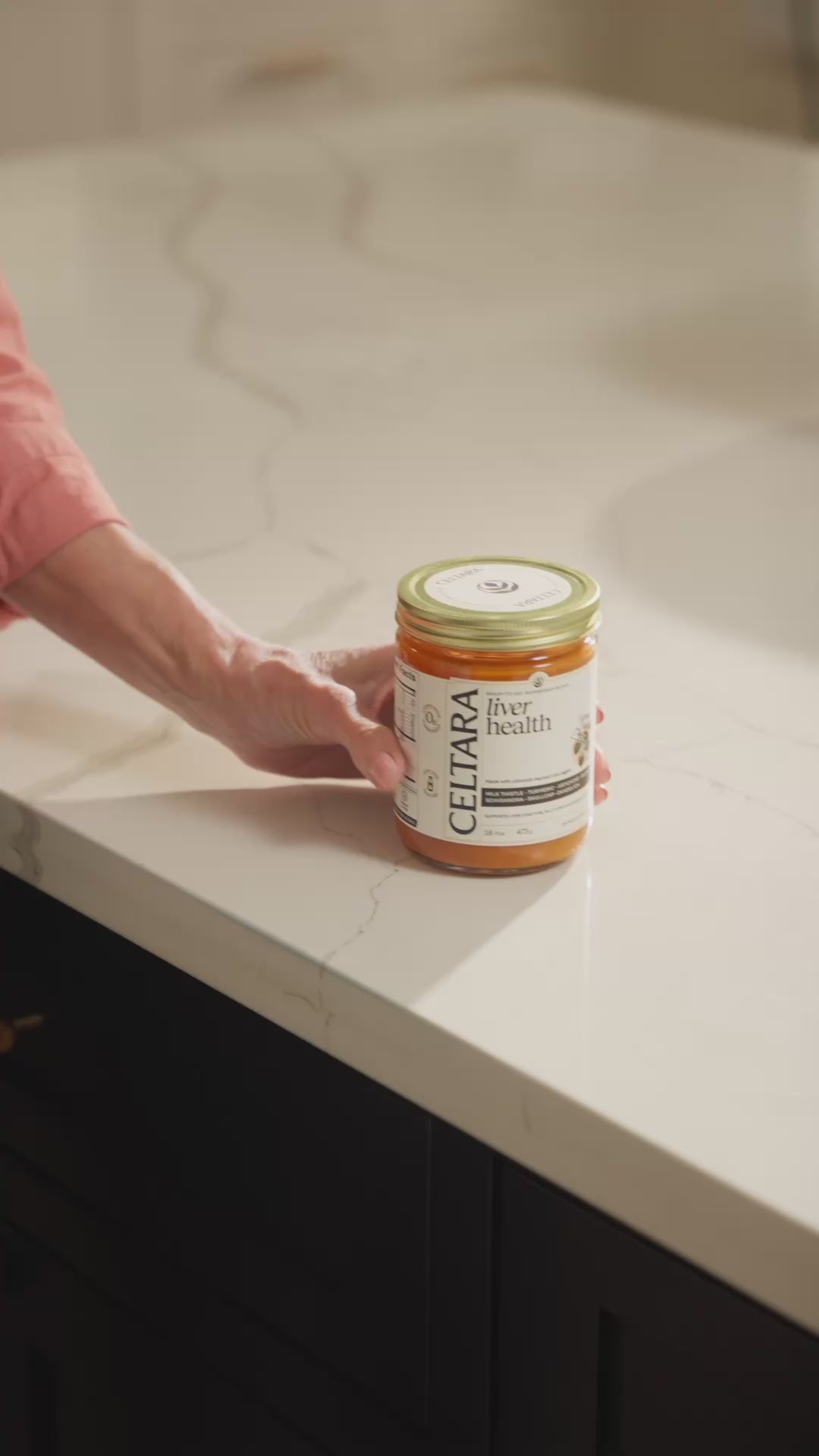 Hand placing a jar of Celtara liver health supplement on a countertop.